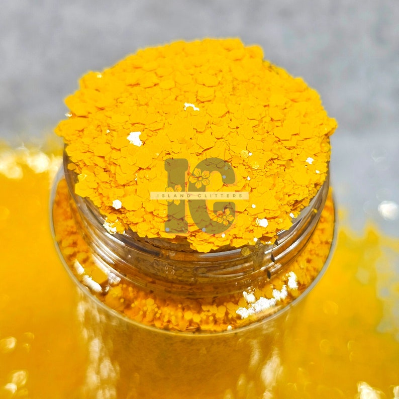 May include: A close-up of a glass jar filled with bright yellow glitter. The jar is labeled "Island Glitters".