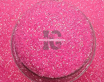 May include: Close-up of a pink glitter eyeshadow with a circular, clear plastic container. The container has the text "IG" printed on it.