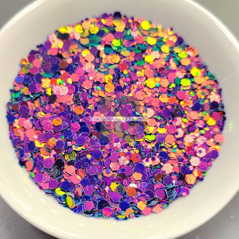 May include: A close-up of iridescent glitter in a variety of shapes and sizes. The glitter is a mix of purple, pink, orange, yellow, and green.