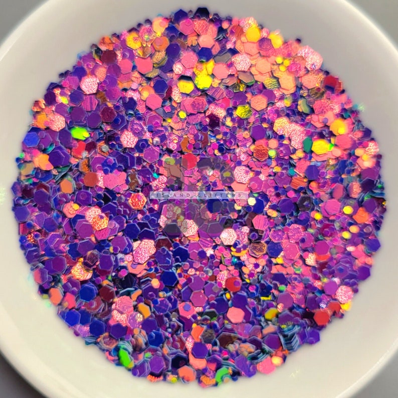 May include: A close-up of a bowl filled with iridescent glitter in shades of pink, purple, and blue. The glitter is in various shapes and sizes, creating a shimmering effect.