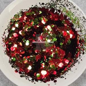 May include: Red, green and black glitter in a white bowl. The glitter is in a variety of shapes and sizes. "Island Glitters" is written in white on the glitter.