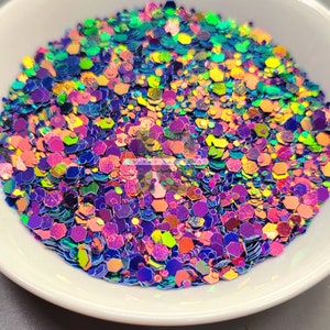 May include: A close-up of iridescent glitter in various shapes and sizes, including hexagons, circles, and squares. The glitter is a mix of blue, green, purple, orange, and yellow.