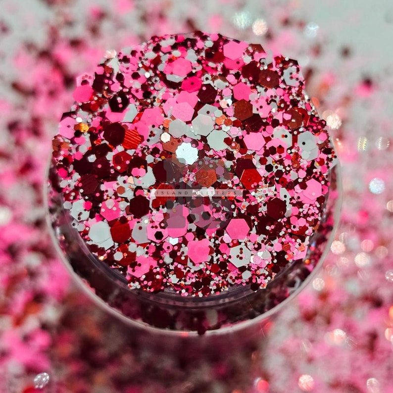 May include: A close-up of a jar filled with pink, red, and white glitter. The glitter is a mix of different shapes and sizes.
