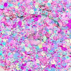 May include: Close-up of a pile of colorful glitter in various shapes and sizes. The glitter is a mix of pink, purple, blue, and iridescent colors. The text "island glitters" is visible in the image.