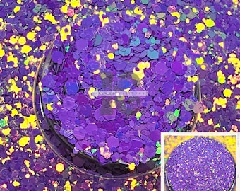 Può includere: Glitter iridescente viola e giallo con finitura olografica. Il glitter è in un barattolo trasparente con un coperchio nero. Il glitter è anche mostrato in un barattolo più piccolo con un coperchio bianco.