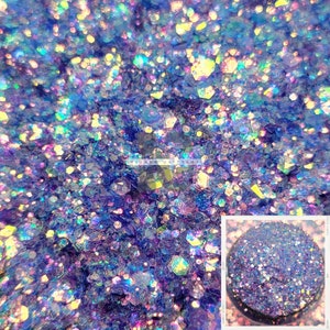 Op de afbeelding: Een close-up van iriserende blauwe, paarse en gouden glitter. De glitter zit in een ronde container met een zwart deksel.