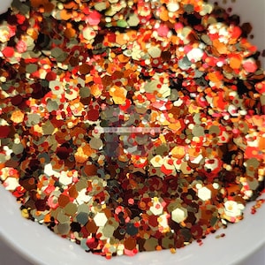 May include: A close-up of a mix of red, orange, gold, and brown glitter. The glitter is in a variety of shapes and sizes.