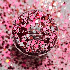 May include: A close-up of a jar filled with pink, red, white, and silver glitter. The glitter is in various shapes and sizes.