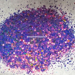 May include: A close-up of a pile of iridescent purple, blue, and pink glitter. The glitter is scattered on a white surface.