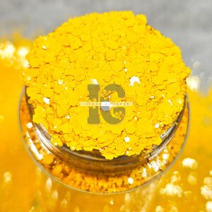 May include: A close-up of a jar filled with bright yellow glitter. The glitter is chunky and has a slight iridescent sheen. The jar is labeled "Island Glitter".