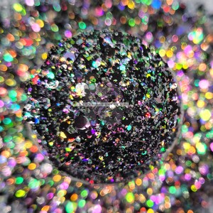 May include: Close-up of black glitter with iridescent sparkles. The glitter is scattered on a surface with a blurred background of colorful iridescent glitter.