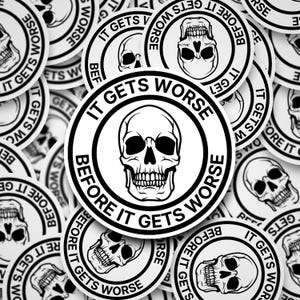 May include: A collection of white circular stickers with a black skull graphic and the text "IT GETS WORSE BEFORE IT GETS WORSE" in a bold, black font. The stickers are scattered across a surface.