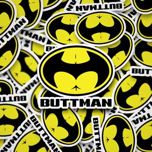 May include: A collection of yellow and black stickers with a parody design. The stickers feature a black bat symbol with a yellow background and the word "BUTTMAN" in a bold, white font. The stickers are scattered across the image.