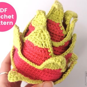 May include: A crocheted pineapple with a green top and a red base. The pineapple is made with yarn and is a handmade craft.