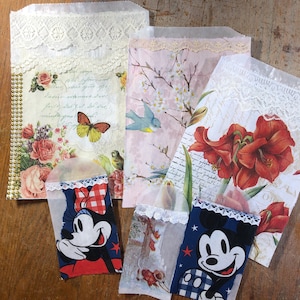May include: Four decorative paper bags with lace trim. The bags feature floral and bird designs. One bag has a red and white Mickey Mouse design. Another bag has a blue and white Mickey Mouse design.