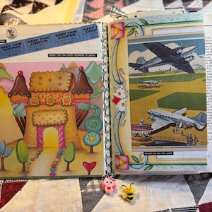 May include: Open journal with colorful illustrations. One page features a whimsical castle made of cookies and ice cream cones. The opposite page displays vintage airplane images. Decorative elements include a blue coupon strip and small, attached charms.