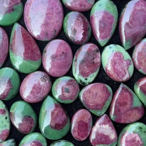 May include: A collection of green and pink gemstone cabochons in a velvet-lined box. The stones are various shapes and sizes, with a mix of green and pink hues.