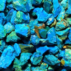 Może przedstawiać: Zbliżenie na kolekcję surowych, naturalnych kamieni turkusowych. Kamienie różnią się rozmiarem i kształtem, prezentując żywą mieszankę odcieni niebieskiego i zielonego. Niektóre kamienie mają brązowe i żółte plamy. Ogólna tekstura jest szorstka i nierówna.