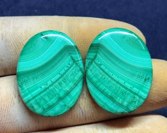May include: Two oval-shaped malachite stones with a vibrant green color and intricate banded patterns. The polished gemstones display varying shades of green, creating a natural, eye-catching design. These stones are ideal for jewelry making.