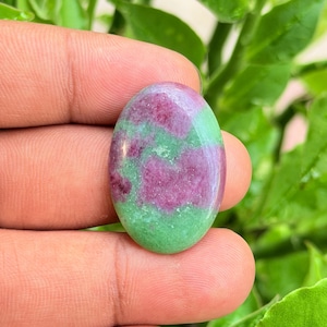 Può includere: Una gemma a cabochon di forma ovale con una superficie lucida caratterizzata da un motivo maculato nei colori rosa magenta vibrante e verde chiaro. La pietra presenta una parte superiore liscia e arrotondata con una finitura lucida.