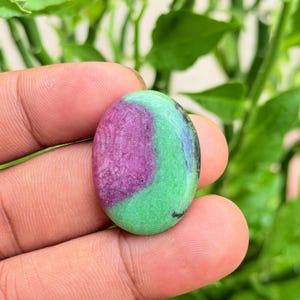 Peut inclure: Une pierre précieuse cabochon de forme ovale présentant une section centrale magenta-rose vibrante contrastée par des zones vert citron vif. La pierre a une surface lisse et polie avec une transition de couleur distincte et des inclusions sombres.