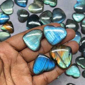 May include: A collection of heart-shaped labradorite gemstones in various shades of blue and green. The stones have a shimmering iridescent effect.