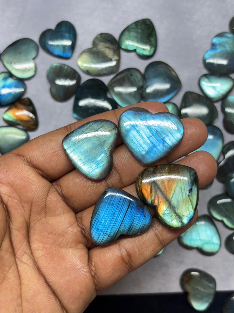 May include: A collection of heart-shaped labradorite gemstones in various shades of blue and green. The stones have a shimmering iridescent effect.
