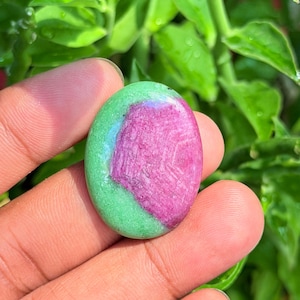 Può includere: Una gemma cabochon di forma ovale caratterizzata da una sezione centrale color rosa magenta vibrante circondata da un bordo liscio verde chiaro. La pietra presenta una superficie lucida e brillante con un netto contrasto di colore.