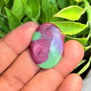 Puede incluir: Una piedra preciosa pulida de forma ovalada con una superficie lisa y una combinación de colores distintiva de rosa magenta vibrante y verde lima claro. La piedra muestra un patrón natural moteado con transiciones de color.