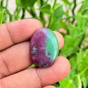 Può includere: Una gemma di rubino zoisite di forma ovale con una superficie lucida e una distinta divisione cromatica. Una metà della pietra è di un rosa magenta intenso, mentre l'altra metà è di un vivace verde lime, con inclusioni naturali visibili.
