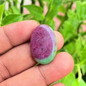 Pode incluir: Uma pedra preciosa em formato de cabochão oval com um centro rosa magenta vibrante de aparência cristalina texturizada, rodeado por uma borda lisa de cor verde-claro sólida. A pedra possui um acabamento polido e brilhante com superfície arredondada.