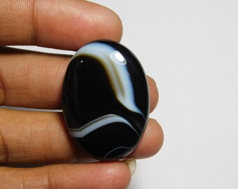 May include: Black and white oval agate cabochon with swirling patterns. The stone has a smooth, polished surface.