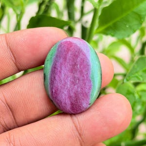 Puede incluir: Una piedra preciosa en forma de cabujón ovalado con un centro de color magenta rosado vibrante rodeado por un borde liso de color verde claro. La piedra tiene una superficie pulida y brillante con inclusiones minerales naturales.