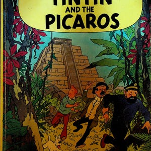 May include: Cover of "The Adventures of Tintin and the Picaros" comic book. The cover features a yellow banner with the title, and illustrations of Tintin, Captain Haddock, and others running from a pyramid in a jungle setting.