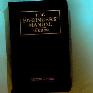 Peut inclure: Un livre noir intitulé "The Engineers' Manual" par Hudson, avec des lettres dorées. La couverture indique également "Second Edition". Le livre est posé sur un fond bleu clair.