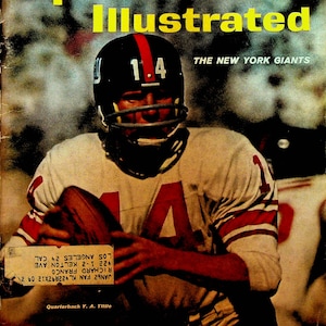 以下が含まれることがあります： 白と赤のジャージを着て、背番号「14」をつけたフットボール選手が写っている、ビンテージのスポーツイラストレイテッド誌の表紙。選手はフットボールを持ってカメラに向かって走っている。雑誌の表紙には「The New York Giants」というタイトルが付けられており、「Sports Illustrated」という文字が黄色で書かれている。