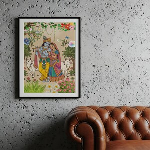 May include: A framed artwork depicting a colorful scene with two figures, possibly deities, in traditional Indian attire. The artwork features a pastoral setting with cows, flowers, and foliage, rendered in vibrant hues of yellow, blue, and pink.