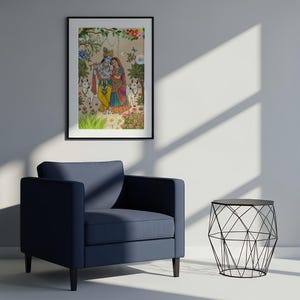 May include: A framed artwork depicts a colorful illustration of two figures in traditional Indian attire, surrounded by flowers and animals. The artwork is displayed above a navy blue armchair and a black wire side table.