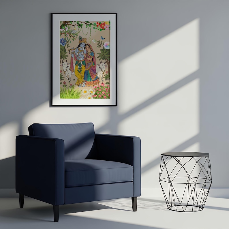 May include: A framed artwork depicts a colorful illustration of two figures in traditional Indian attire, surrounded by flowers and animals. The artwork is displayed above a navy blue armchair and a black wire side table.