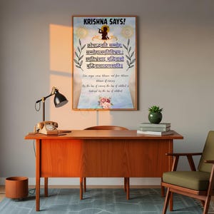 May include: A framed poster with the text "KRISHNA SAYS!" in blue, featuring Sanskrit text and English translation. The poster is on a wooden desk with a vintage telephone, a lamp, and a small plant. The room has a neutral color palette.
