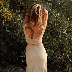 Puede incluir: Un conjunto de dos piezas verde oliva claro, que consta de un top corto y una falda larga. La modelo est&aacute; de pie frente a un fondo de hojas verdes. Un tatuaje es visible en la espalda de la modelo. El logotipo "CARIK GANG" est&aacute; en la esquina inferior izquierda.
