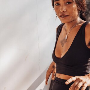 Puede incluir: Una mujer con un top corto y pantalones cortos negros. Tiene un collar y pendientes de plata. La mujer tiene tatuajes y un piercing en la nariz. La imagen est&aacute; tomada con luz natural.