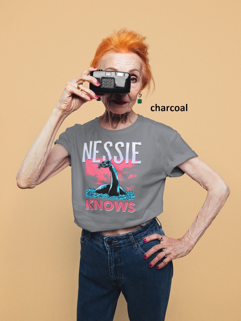 May include: A charcoal grey t-shirt with a graphic of a Loch Ness Monster and the text "Nessie Knows".
