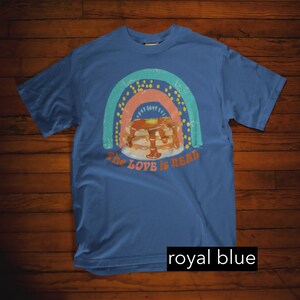 Puede incluir: Una camiseta azul real con un gr&aacute;fico de arco&iacute;ris de estilo vintage y una pila de panqueques con jarabe. El texto "The Love is Real" est&aacute; impreso debajo de los panqueques.