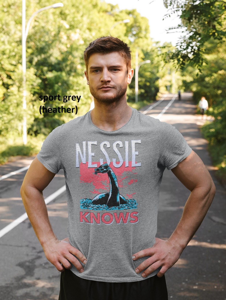 May include: A heather grey t-shirt with a graphic of Nessie, the Loch Ness Monster, and the text "Nessie Knows".