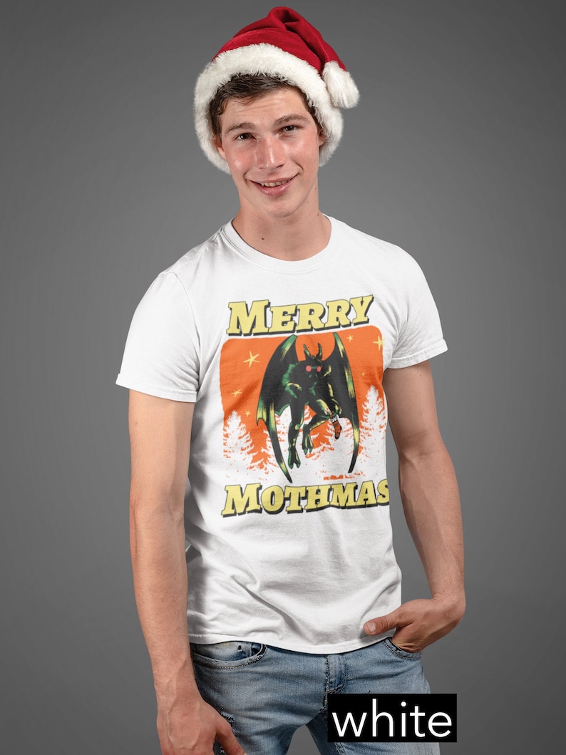 May include: A white t-shirt with a green monster graphic and the text "Merry Mothmas". The person wearing the shirt is also wearing a red Santa hat.