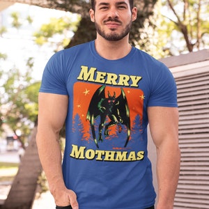 May include: A royal blue t-shirt with a graphic of a green monster with red eyes and wings. The graphic is surrounded by a yellow border and the text "Merry Mothmas" in yellow letters.