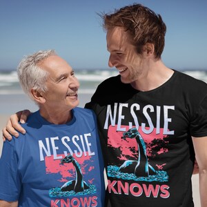 May include: Two people wearing blue and black t-shirts with a graphic of a Loch Ness Monster and the text "Nessie Knows".