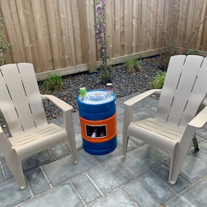 Op de afbeelding: Twee beige Adirondack-stoelen met een blauwe en oranje koeler met het Oilers-logo erop als tafel ertussen. De koeler heeft een ingebouwde flesopener en een plek om drankjes op te bergen.