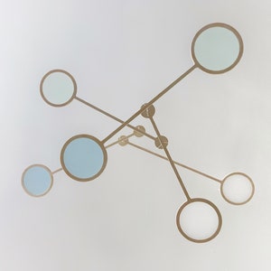 May include: A modern light fixture with six circular light shades. The shades are made of glass and are suspended from a metal frame. The shades are a light blue colour and the frame is a gold colour.